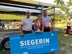 Drei Ruder*innen halten Uni-Cup-Pokal und das blaue Schild mit der Aufschrift Siegerin